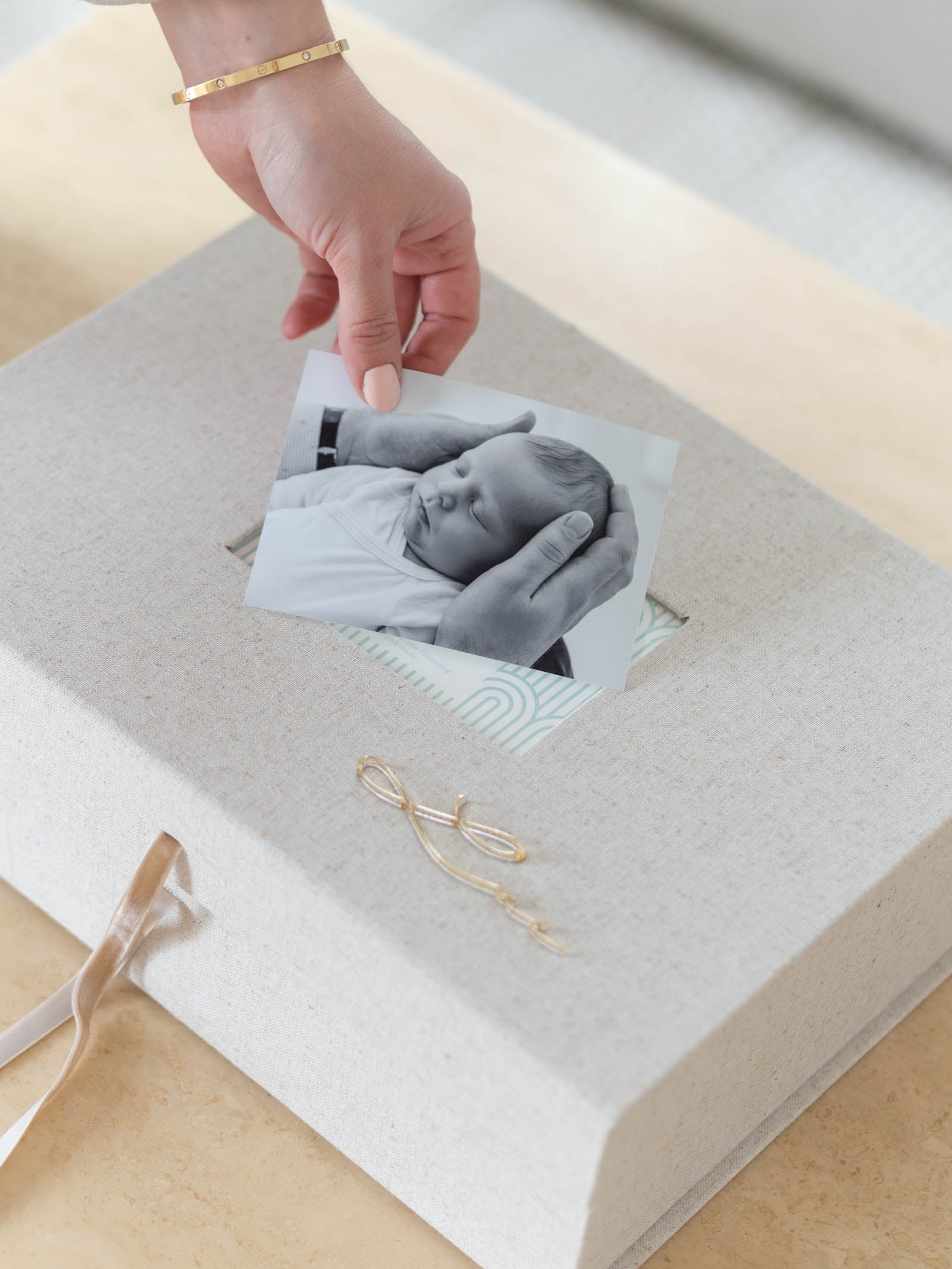 Hand hält Babyfoto an Baby Erinnerungsbox aus Leinen