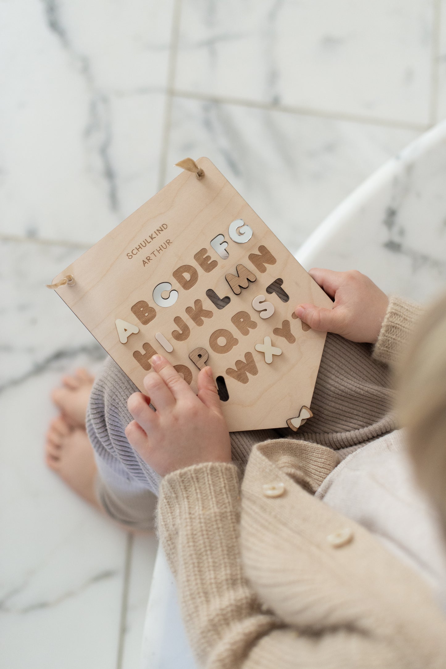 Kinderhände halten personalisierten ABC Wimpel und fahren die Buchstaben nach